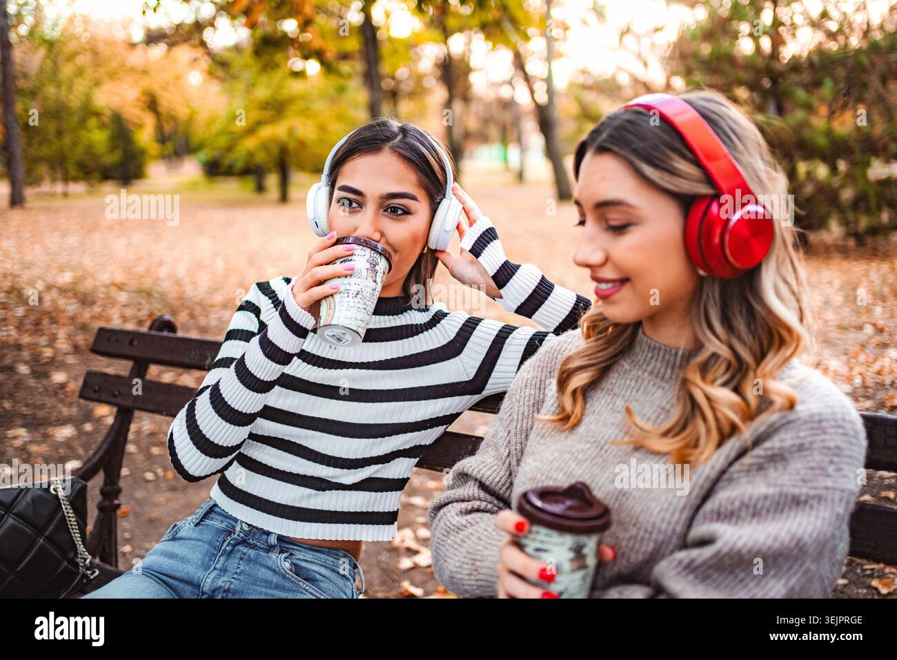 Due ragazze si godono le vibrazioni autunnali sorseggiando bevande calde nel parco Foto Stock