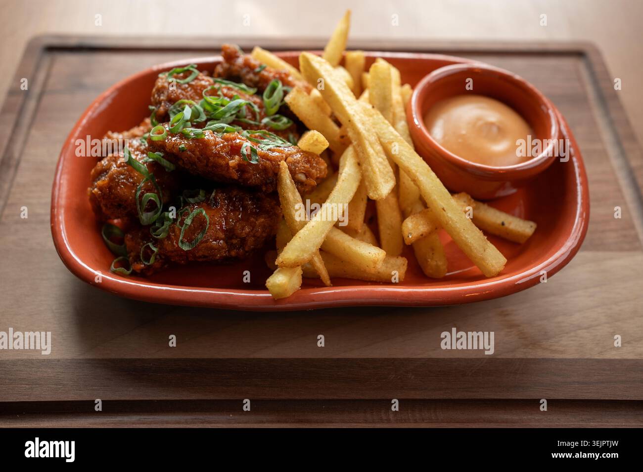 Ali di pollo croccanti servite con patatine fritte dorate e salsa piccante Foto Stock