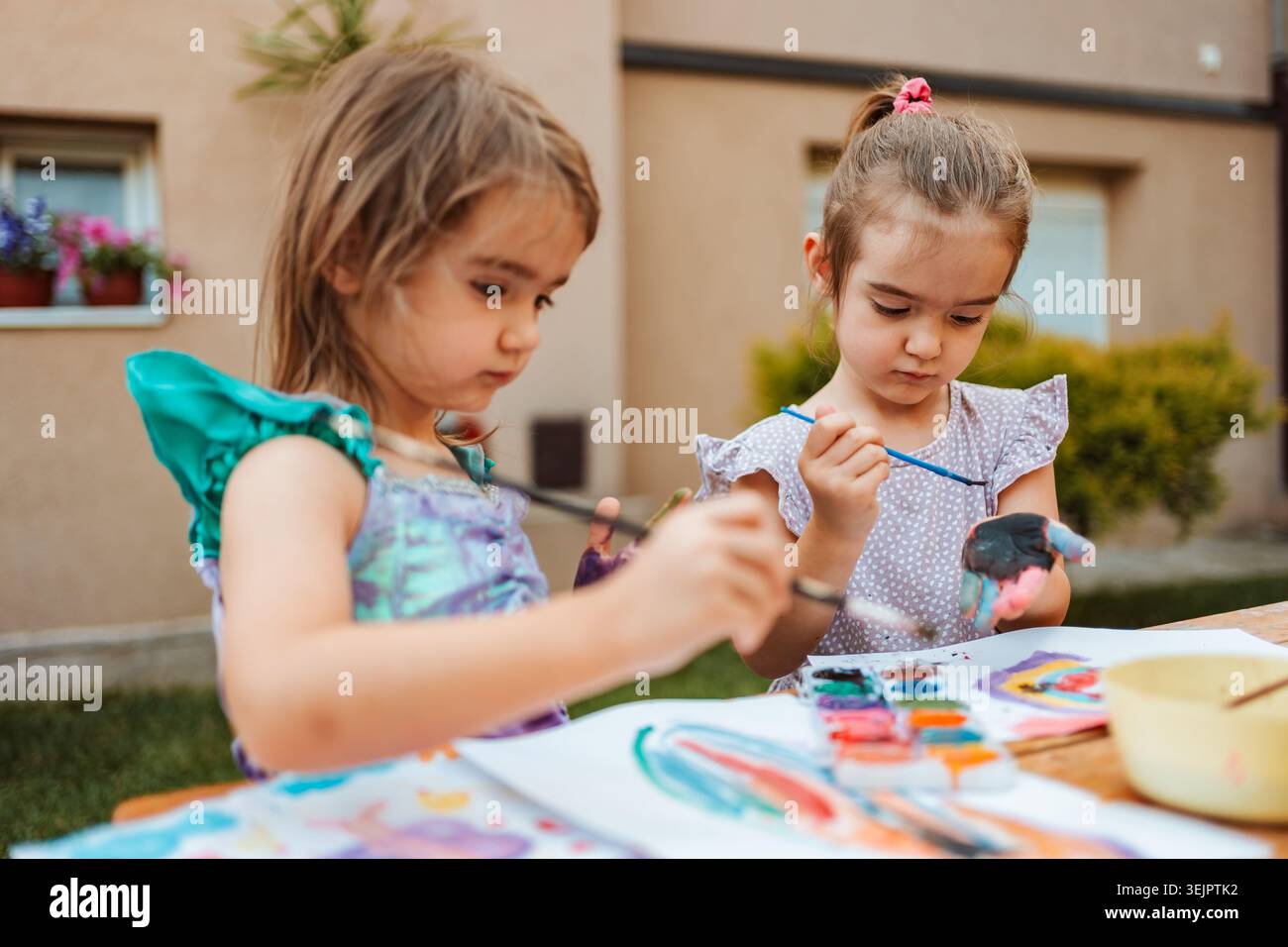 Due ragazze in età prescolare che dipingono con acquerelli nel cortile posteriore Foto Stock