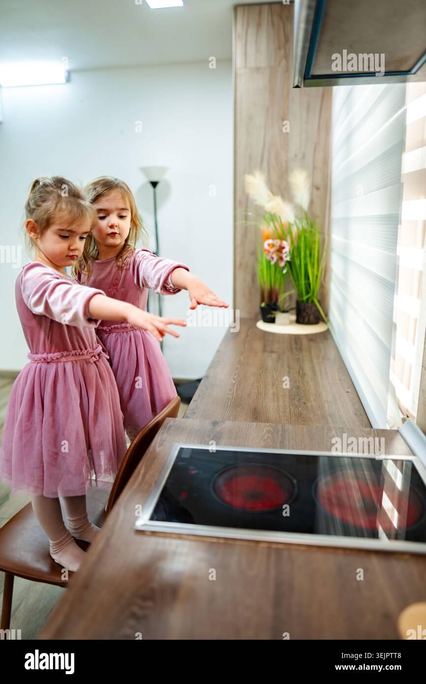 Due ragazze curiose esplorano una cucina moderna con tecnologia di cottura interattiva durante un luminoso pomeriggio di gioco Foto Stock