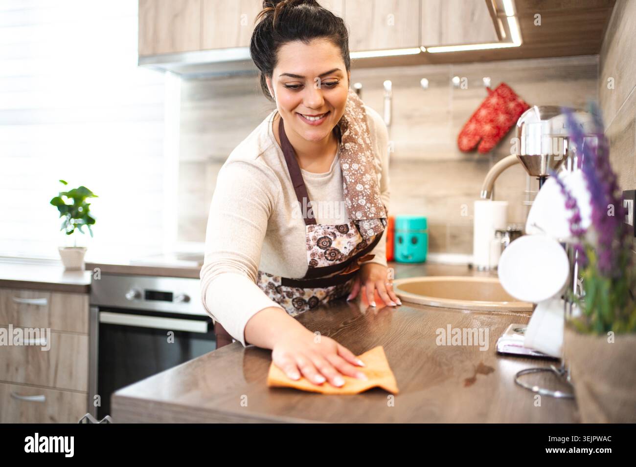 Donna in grembiule che pulisce il bancone della cucina Foto Stock