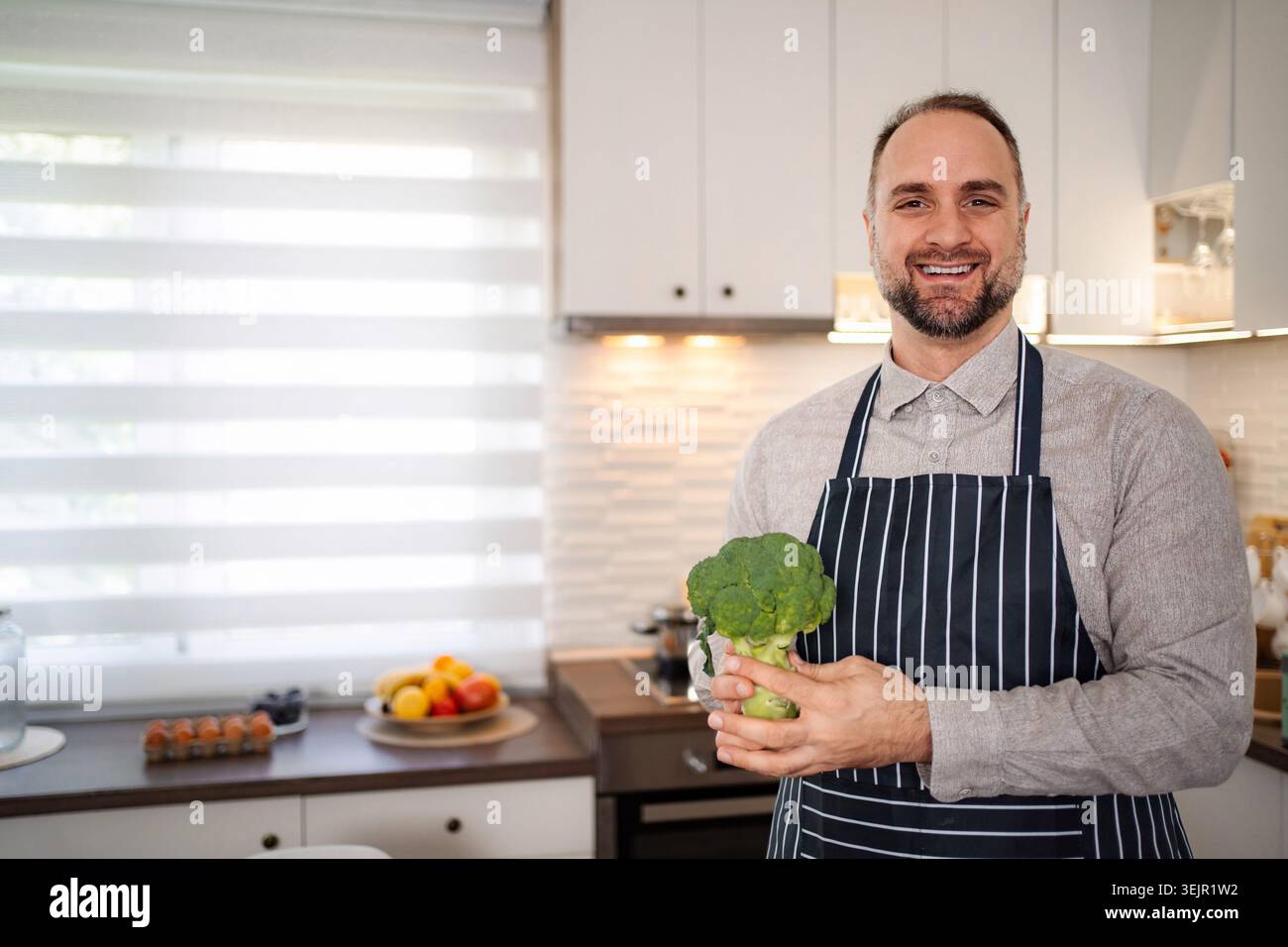 Lo chef sorridente che tiene in cucina broccoli freschi Foto Stock