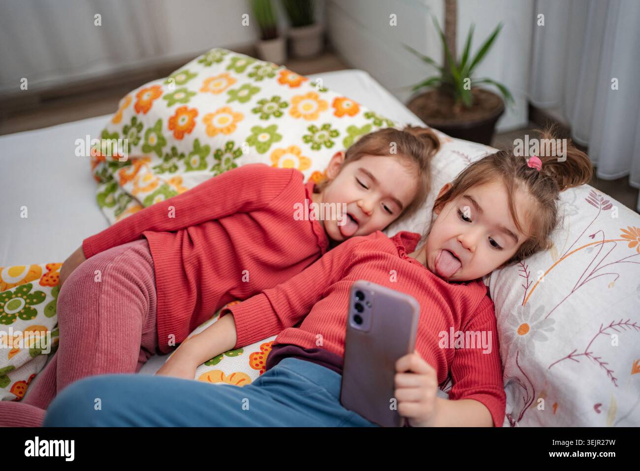 Ragazze gemelle che fanno facce divertenti scattando selfie su smartphone Foto Stock