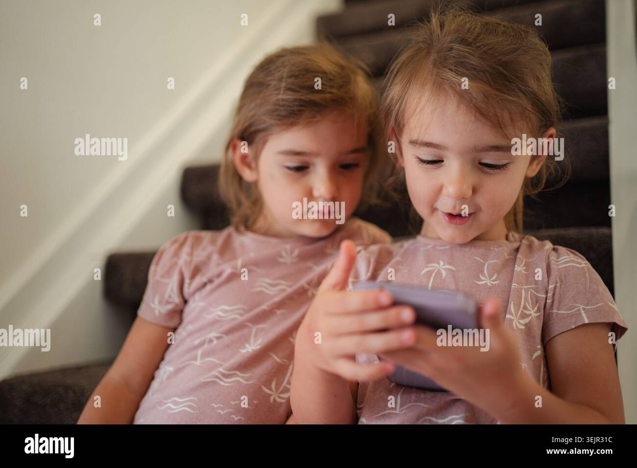 Due ragazze in età prescolare che usano uno smartphone seduto sulle scale di casa Foto Stock