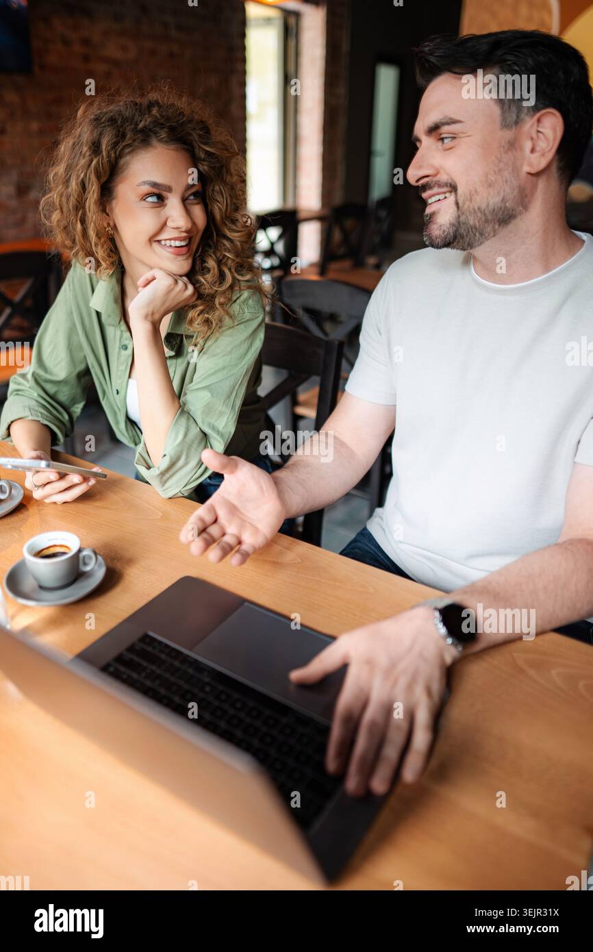 Giovane coppia felice che parla e lavora al computer portatile in un bar Foto Stock