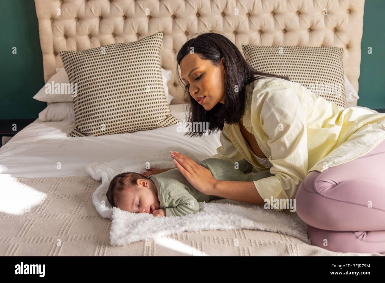 Madre e neonato afroamericani, mamma inginocchiata sul letto che si appoggia sul neonato addormentato vicino alla testata. Baby, badante, nutrire Foto Stock