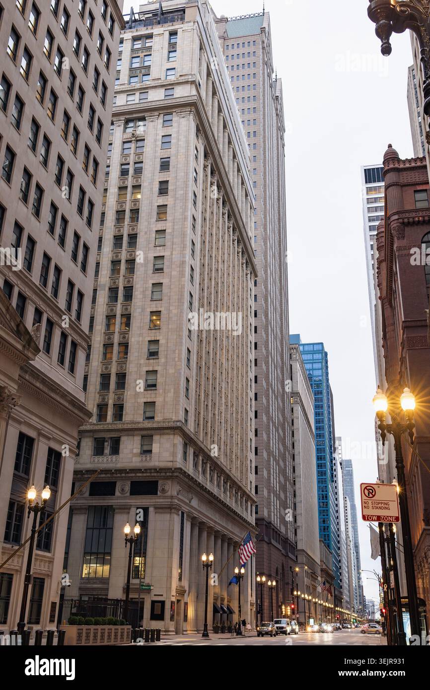 Edifici alti fiancheggiano le strade del centro di Chicago. Il cielo è grigio e le nuvole coprono la città. Le auto si muovono lentamente mentre le persone camminano sul marciapiede. Foto Stock
