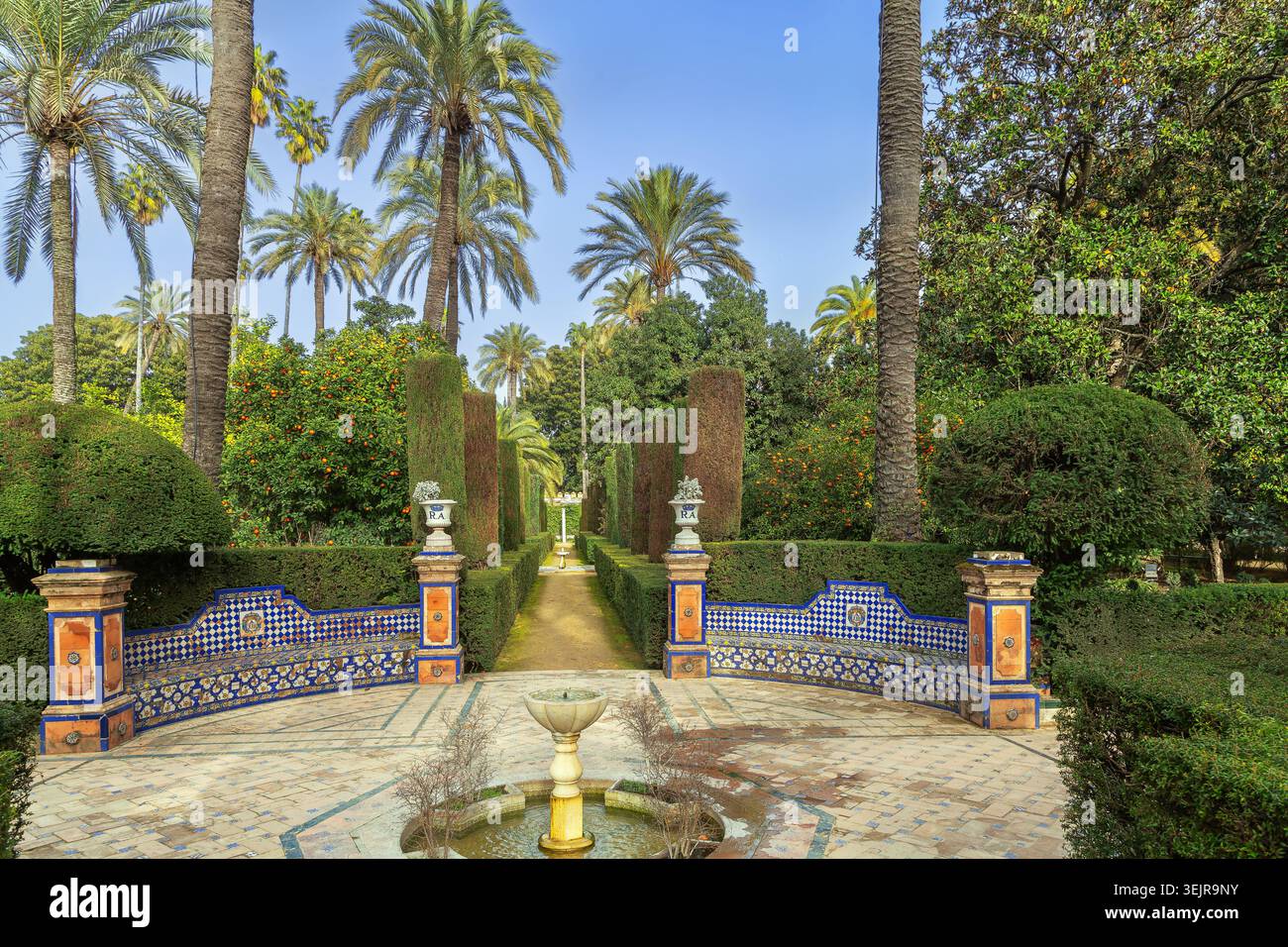 Vicolo decorativo nei giardini dell'Alcazar di Siviglia, Spagna, con una piccola fontana. Panchine piastrellate in ceramica sotto il cielo azzurro Foto Stock
