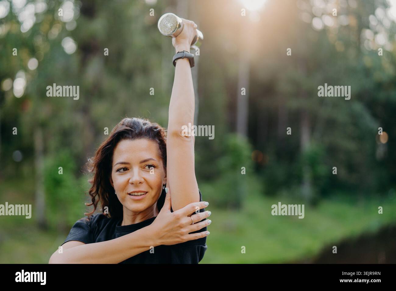 Donna che allunga il braccio con il manubrio durante l'allenamento all'aperto nel parco forestale Foto Stock