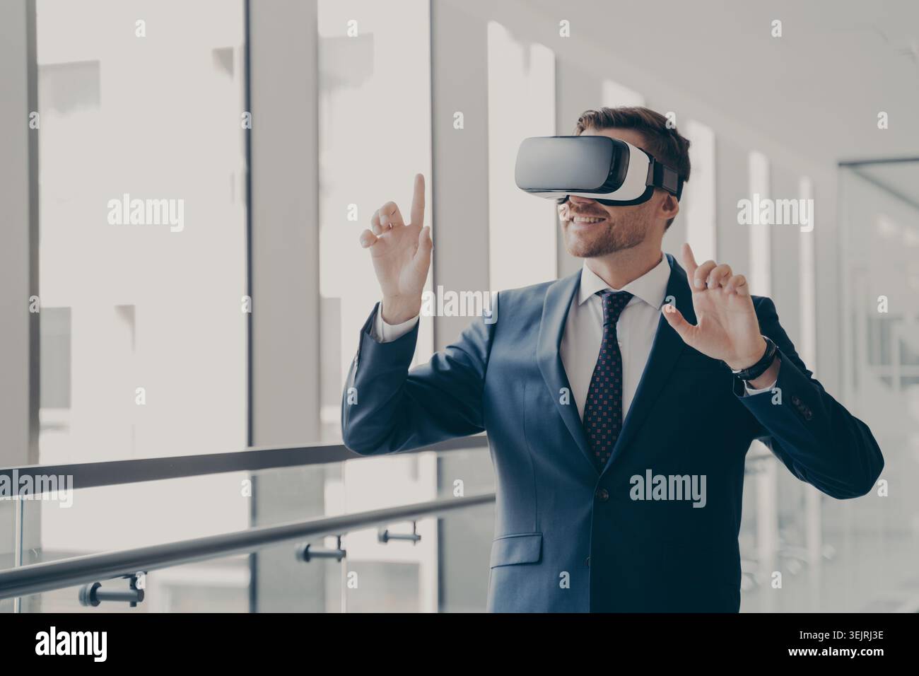 Uomo d'affari che indossa i gesti del visore per la realtà virtuale in un moderno corridoio d'ufficio Foto Stock