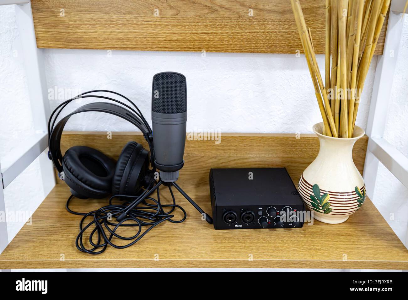 Un impianto di registrazione audio è disposto su un ripiano in legno che include un microfono a condensatore nero su un piccolo supporto per treppiede e un paio di cuffie a una a digitale Foto Stock