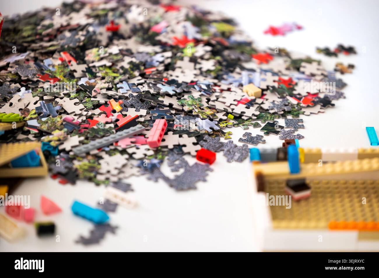 Un mucchio indifferenziato di pezzi di puzzle in cartone giace su una superficie bianca accanto a più mattoni di plastica da costruzione ed elementi sotto B. Foto Stock