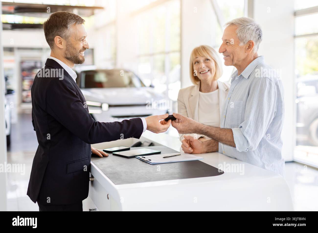 Venditore di auto professionale che consegna la chiave del veicolo a una coppia di clienti senior soddisfatta Foto Stock