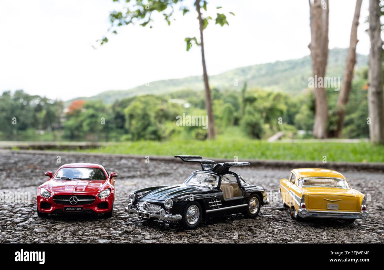 Chiang mai, Thailandia - 25 maggio 2026 : tre modelli di auto in metallo pressofuso rosso AMG GT nero Mercedes 300SL 1954 e giallo 57 Chevy su strada ghiaia all'aperto Foto Stock