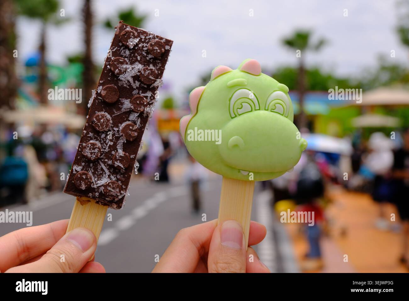 Shanghai, Cina - 30 maggio 2026: Due mani che reggono un gelato LEGO a forma di mattone e un gelato a forma di dinosauro a Legoland Foto Stock