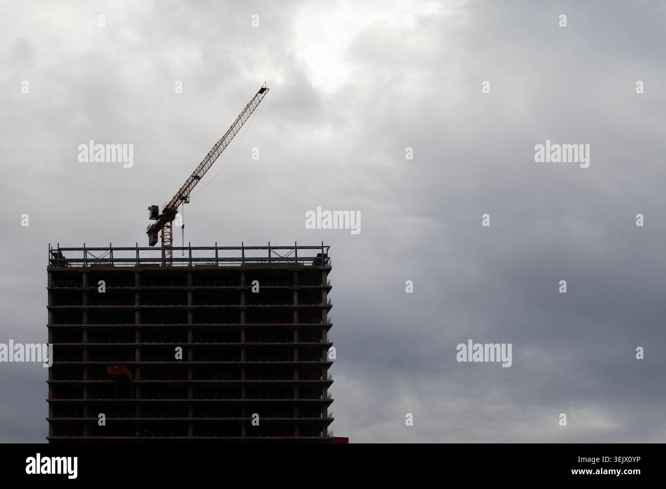 Alta silhouette da costruzione con una gru sopra il cielo nuvoloso Foto Stock