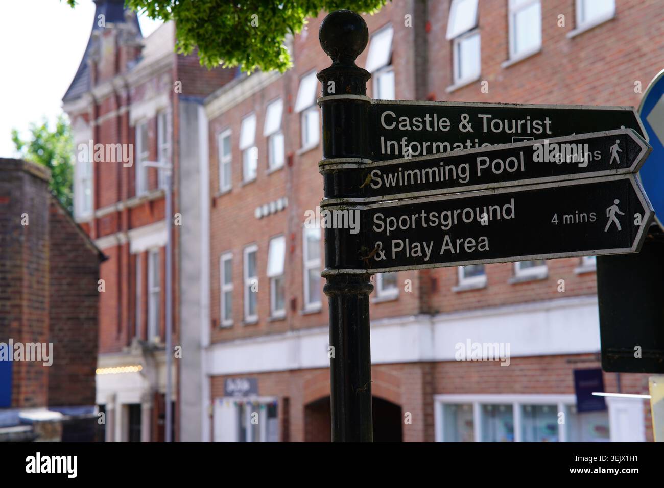 Segnaletica nera direzionale che mostra la strada per il castello, informazioni turistiche, piscina e campo sportivo nella soleggiata strada cittadina britannica. Foto Stock