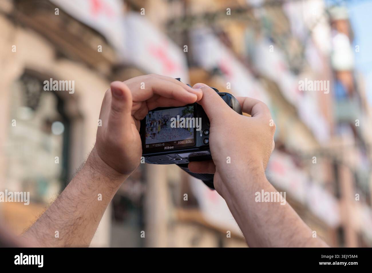Mani di un fotografo in possesso di una fotocamera digitale che mostra una parata sul suo schermo durante il Festival di Alcoy il 26 aprile 2026, Spagna Foto Stock