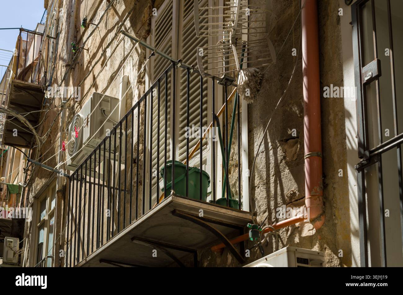 I residenti di questo stretto balcone dell'appartamento utilizzano lo spazio per le faccende quotidiane, riponendo uno spazzolone, un secchio e un portabagagli per gestire il loro ambiente di vita limitato Foto Stock