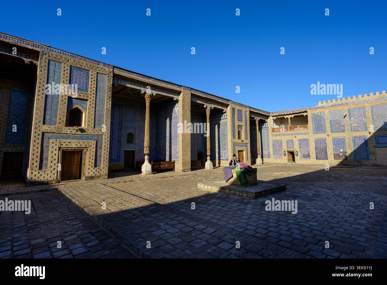 Cortile Harem del Palazzo Toshhovli con Wifes Aiwans e donna uzbeka che vendono tessuti a Khiva, Uzbekistan Foto Stock