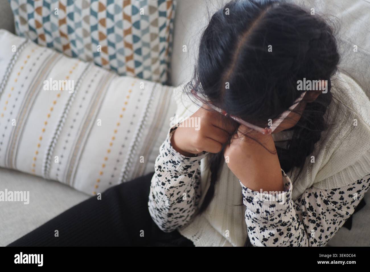 Il bambino siede sul divano con le mani sul viso in un ambiente domestico Foto Stock