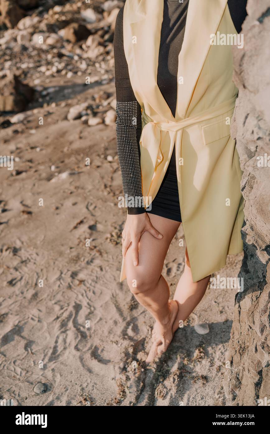 Gilet da spiaggia donna in piedi sulla spiaggia sabbiosa vicino a rocce con gilet giallo e top nero scintillante con spazio per le copie Foto Stock