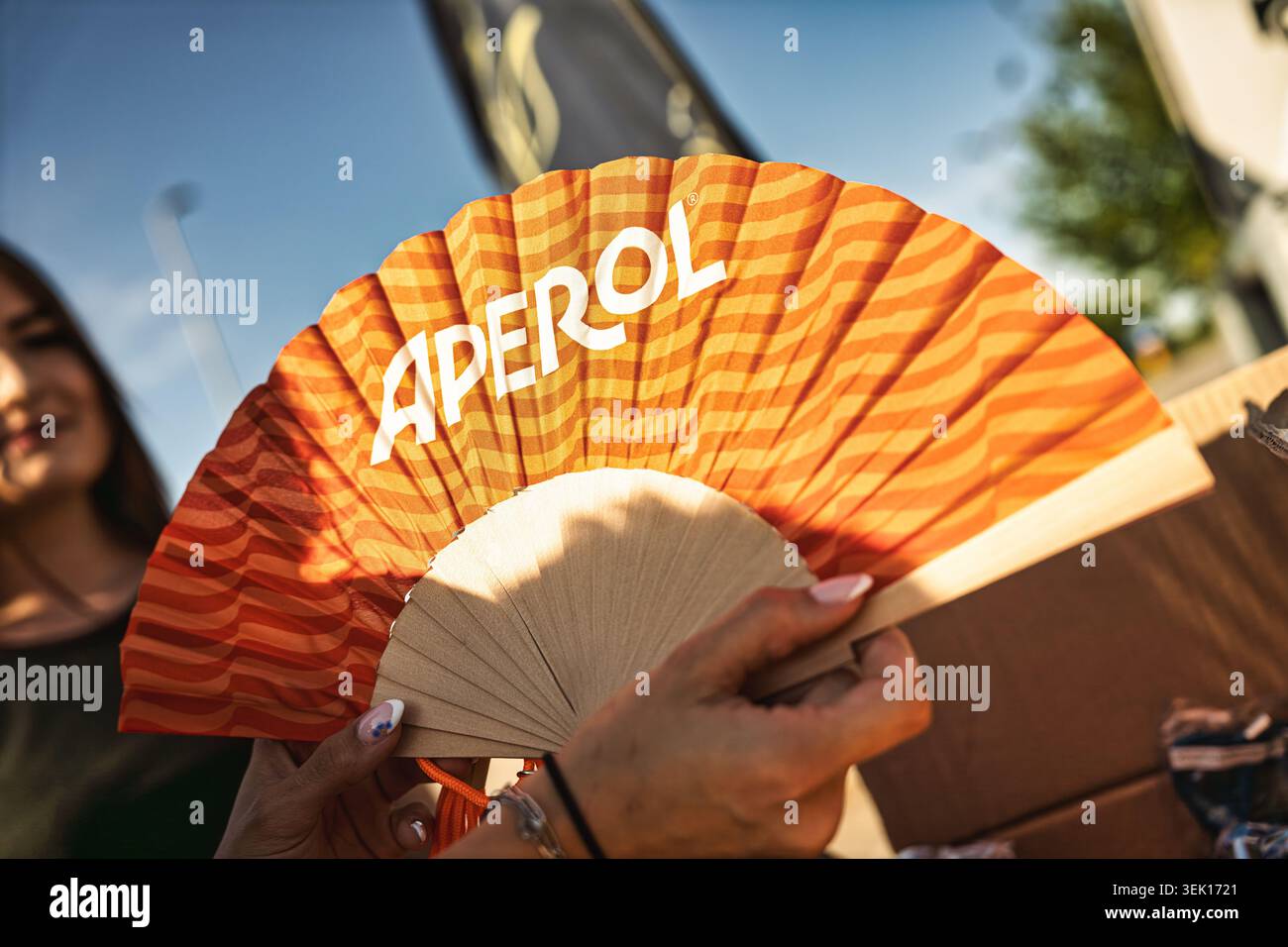 Roma, italia 29 maggio 2026: Persona che detiene un ventilatore a mano a marchio aperol in occasione di un evento estivo all'aperto, concorso promozionale per il raffreddamento dei partecipanti, arancione brillante Foto Stock