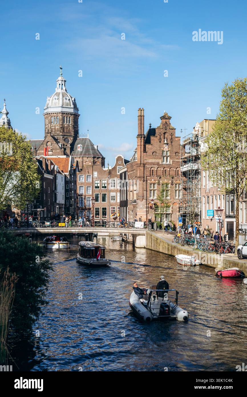 Amsterdam, Paesi Bassi - 18 aprile 2026: Soleggiate vedute primaverili dei canali di Amsterdam con barche turistiche, storici edifici olandesi e l'iconico Ba Foto Stock