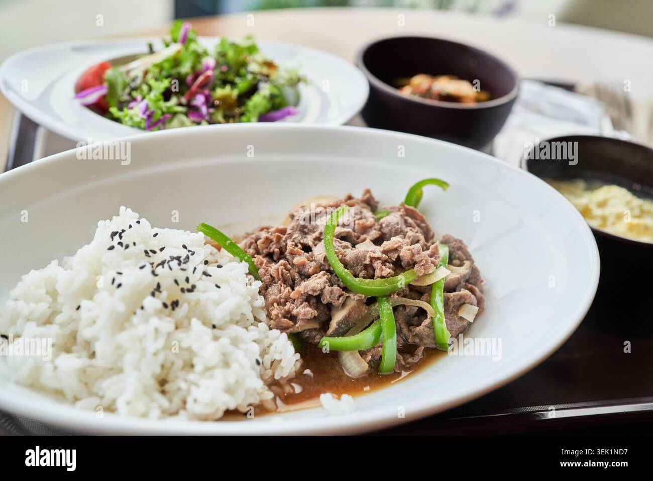 Ciotola di riso bulgogi di manzo coreano con manzo marinato salato, peperoni verdi e riso in un piatto bianco, completo di insalata e contorni. Foto Stock
