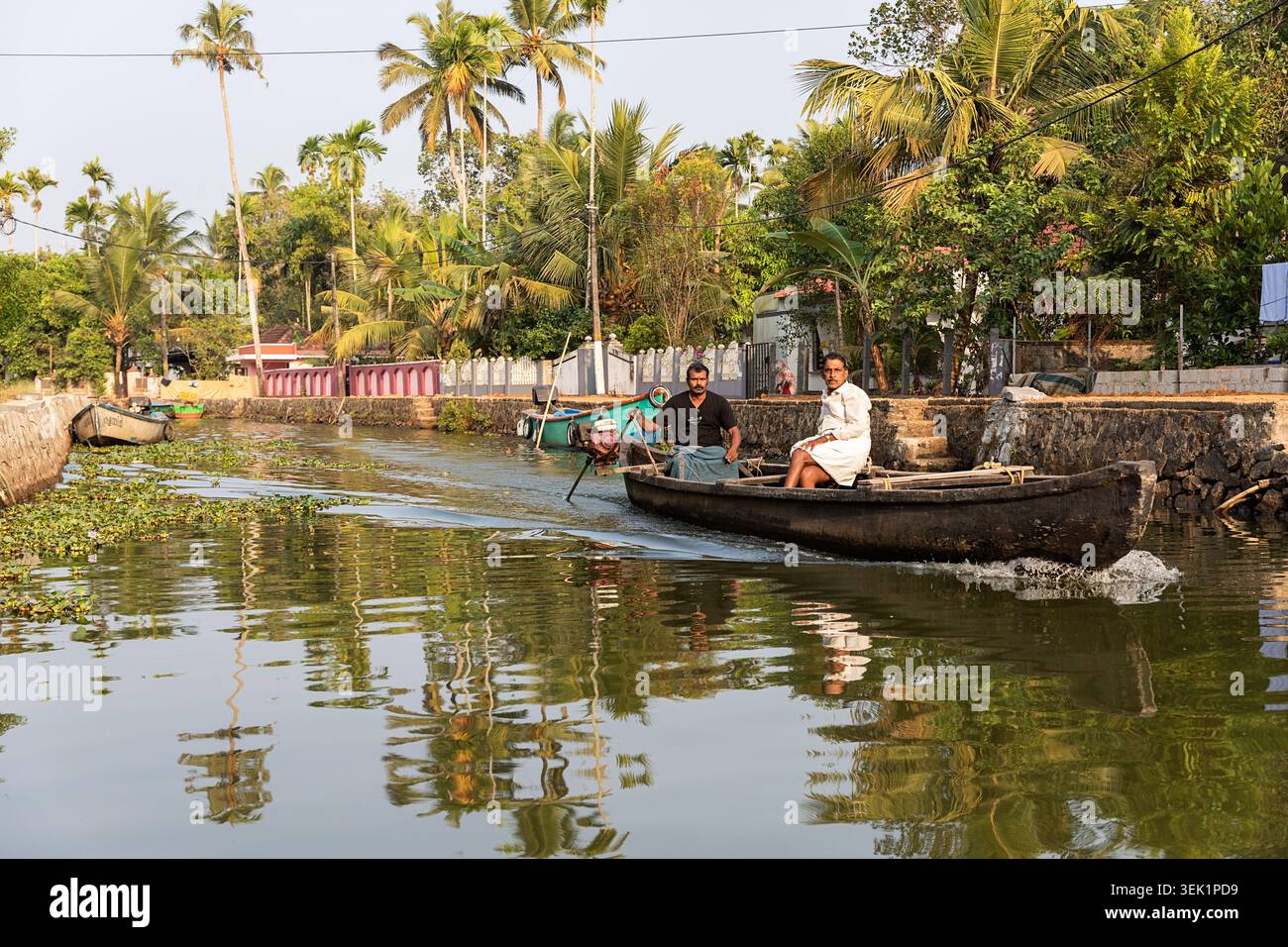 Uomini del posto a bordo di una tradizionale barca di legno nelle acque secondarie vicino ad Alleppey nel Kerala, barcaiolo come tassista che trasporta merci e persone locali Foto Stock