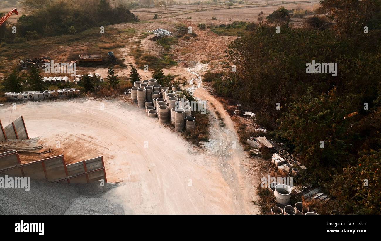Cantiere di materiali da costruzione con tubi in cemento, pali di ghiaia e vista sul paesaggio rurale Foto Stock