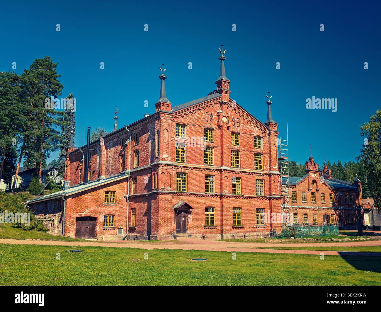 Kouvola, Finlandia - 16.08.2020: Grande fabbrica di mattoni d'epoca caratterizzata da torrette ornate e cornici gialle per finestre in mezzo al verde paesaggio Foto Stock