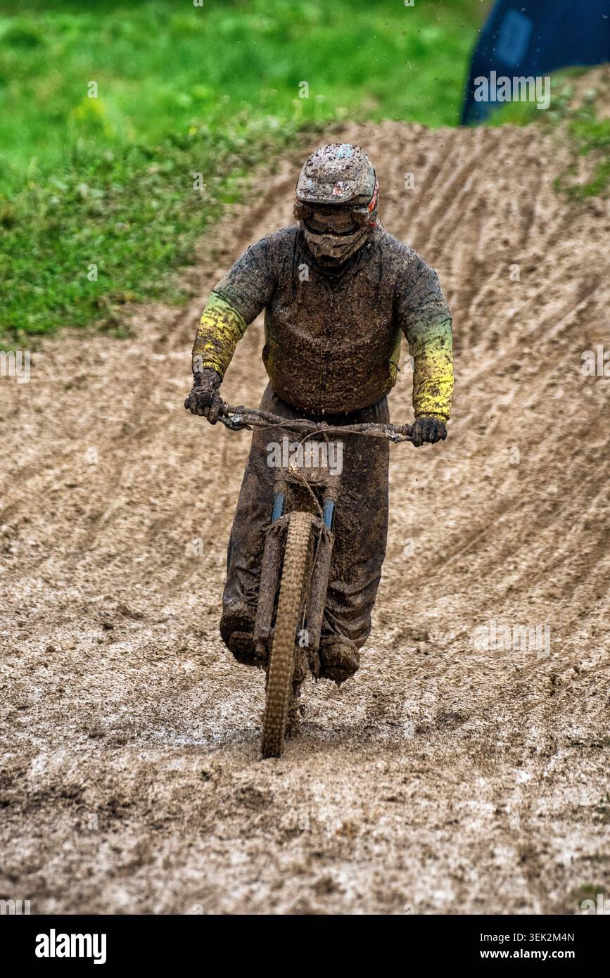 Le escursioni in mountain bike coperte di fango attraversano un sentiero bagnato in condizioni meteorologiche difficili. Scene all'aperto ricche di azione che mettono in risalto resistenza e determinazione Foto Stock