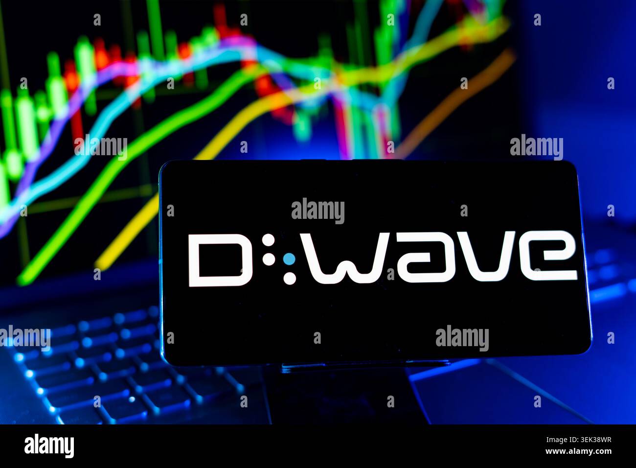 Logo D Wave Quantum visualizzato sul telefono cellulare con sfondo grafico delle prestazioni del mercato azionario e interfaccia grafico di trading Foto Stock