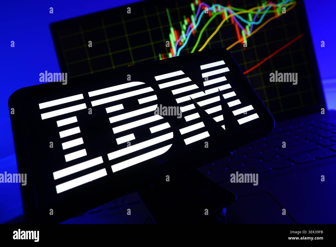 Logo IBM visualizzato sul telefono cellulare con sfondo grafico delle prestazioni del mercato azionario e interfaccia grafico di trading Foto Stock