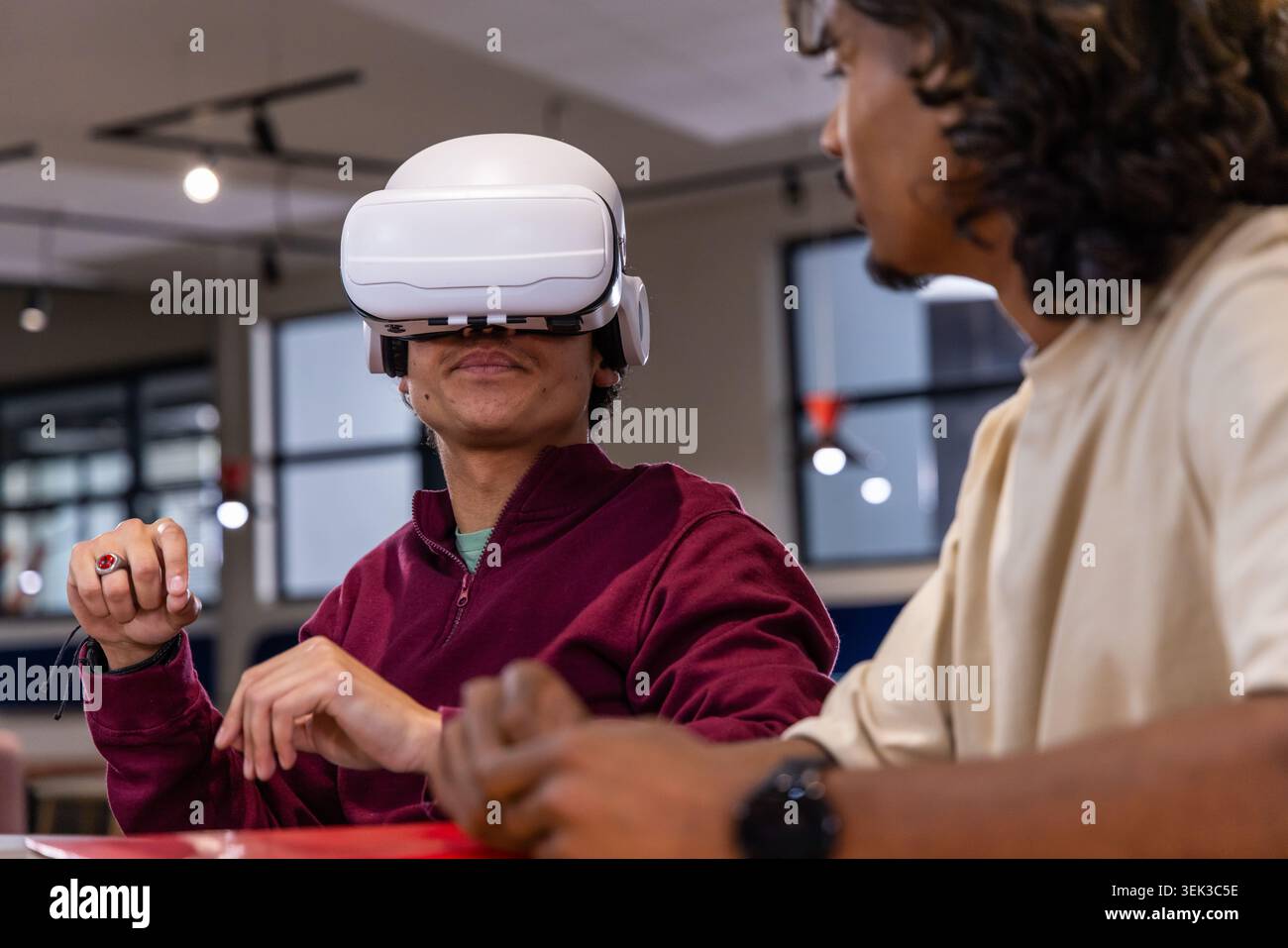 Diversi coetanei maschi gestiscono e interagiscono con il visore VR bianco e il maglione marrone nello spazio di studio Foto Stock