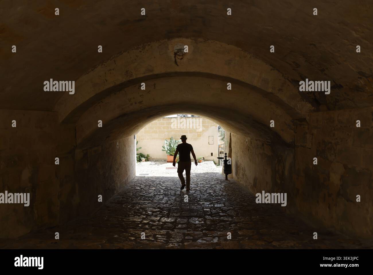 Turista che passa sotto un'antica arcata in una città medievale, con retroilluminazione e contrasto drammatici che creano un concetto di viaggio ed esplorazione Foto Stock