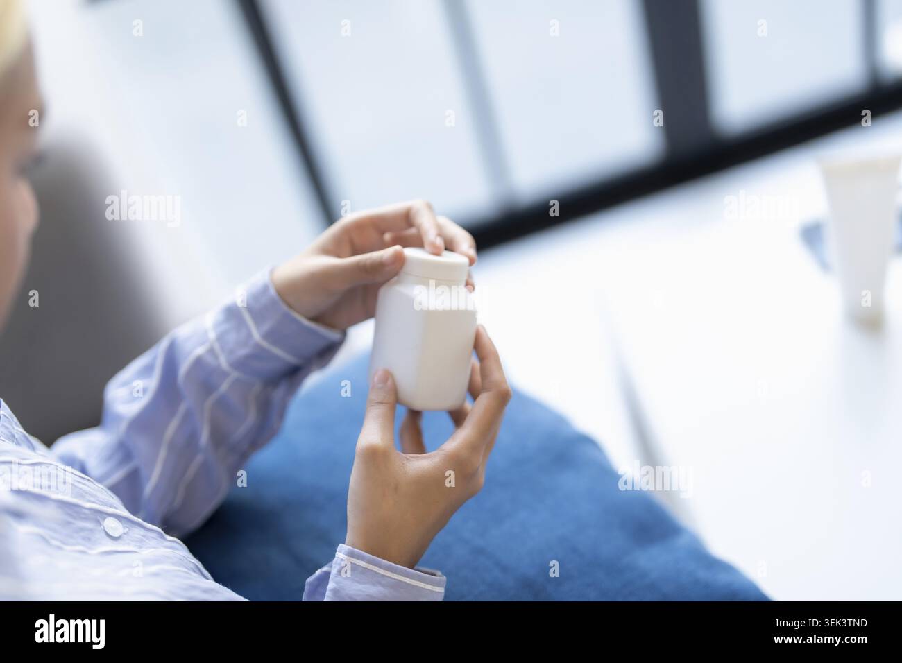 Donna asiatica in procinto di prendere vitamine dalla bottiglia, cura di sé e benessere a casa Foto Stock