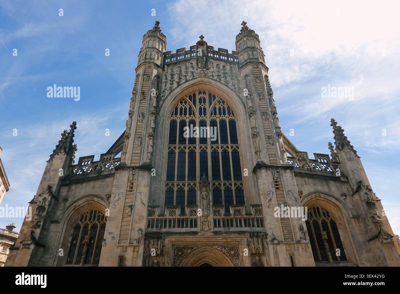 Vista architettonica dall'angolo basso della grandiosa facciata del fronte occidentale dell'Abbazia di Bath con le sue grandi vetrate colorate a Bath, Somerset, Regno Unito Foto Stock