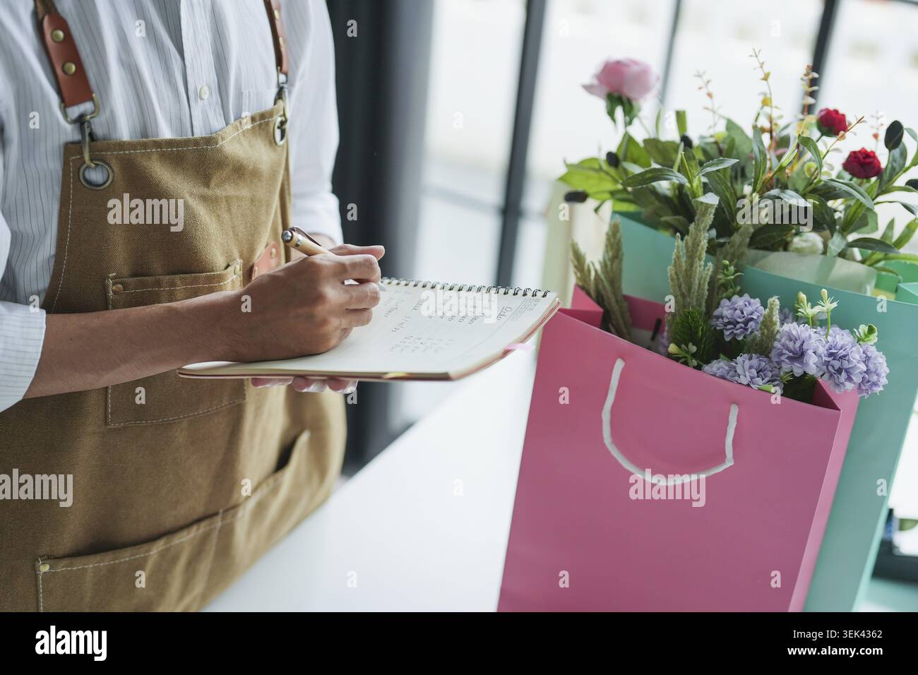 Il proprietario di una piccola azienda asiatica di un negozio di fiori e piante rispettose dell'ambiente consegna con gioia piante fresche in vaso e fiori in fiore bou Foto Stock