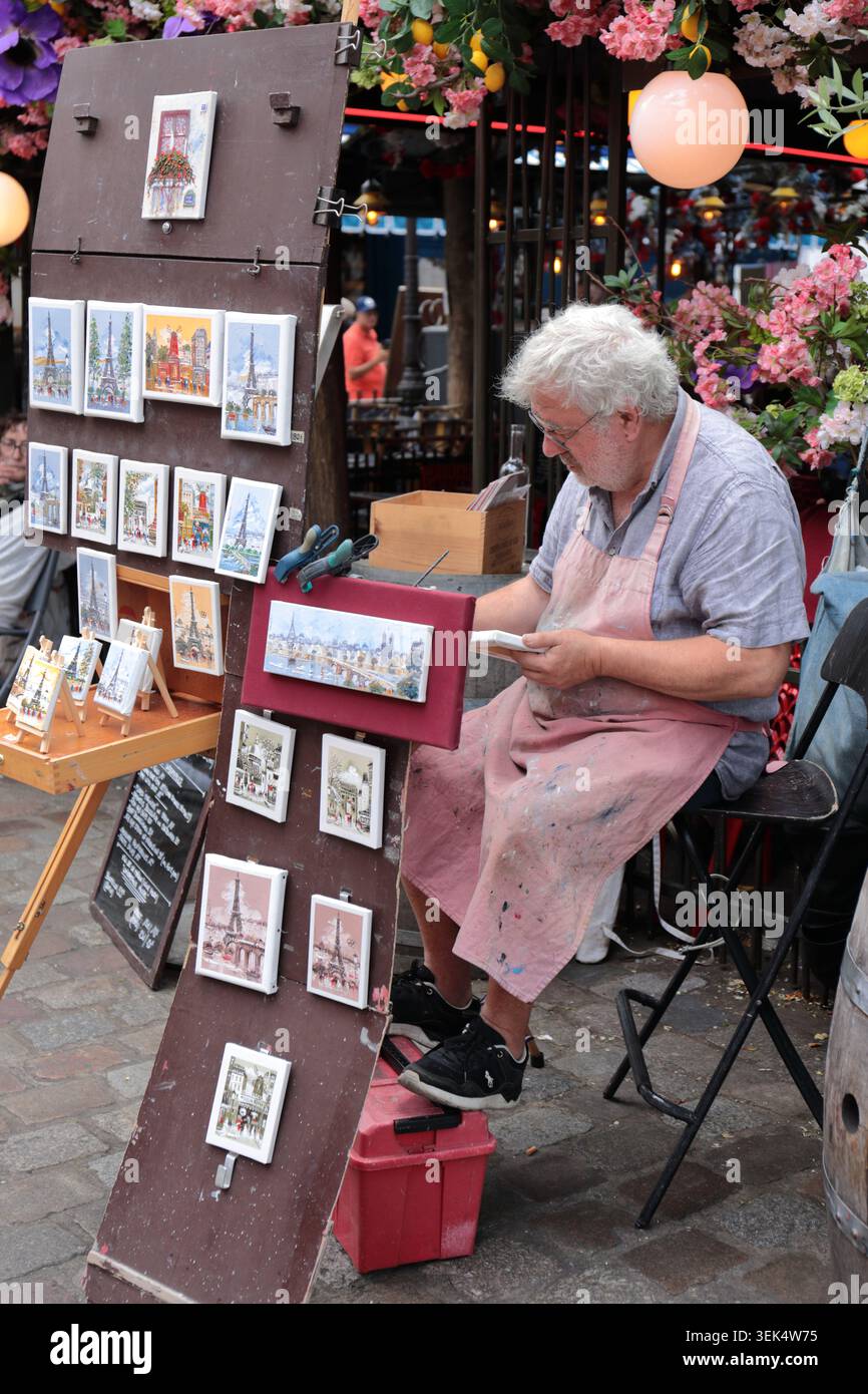 Parigi, Francia - 9 agosto 2024: Vecchio pittore di strada che crea opere d'acquerello e vende dipinti fatti a mano in un vivace mercato all'aperto di Parigi Foto Stock