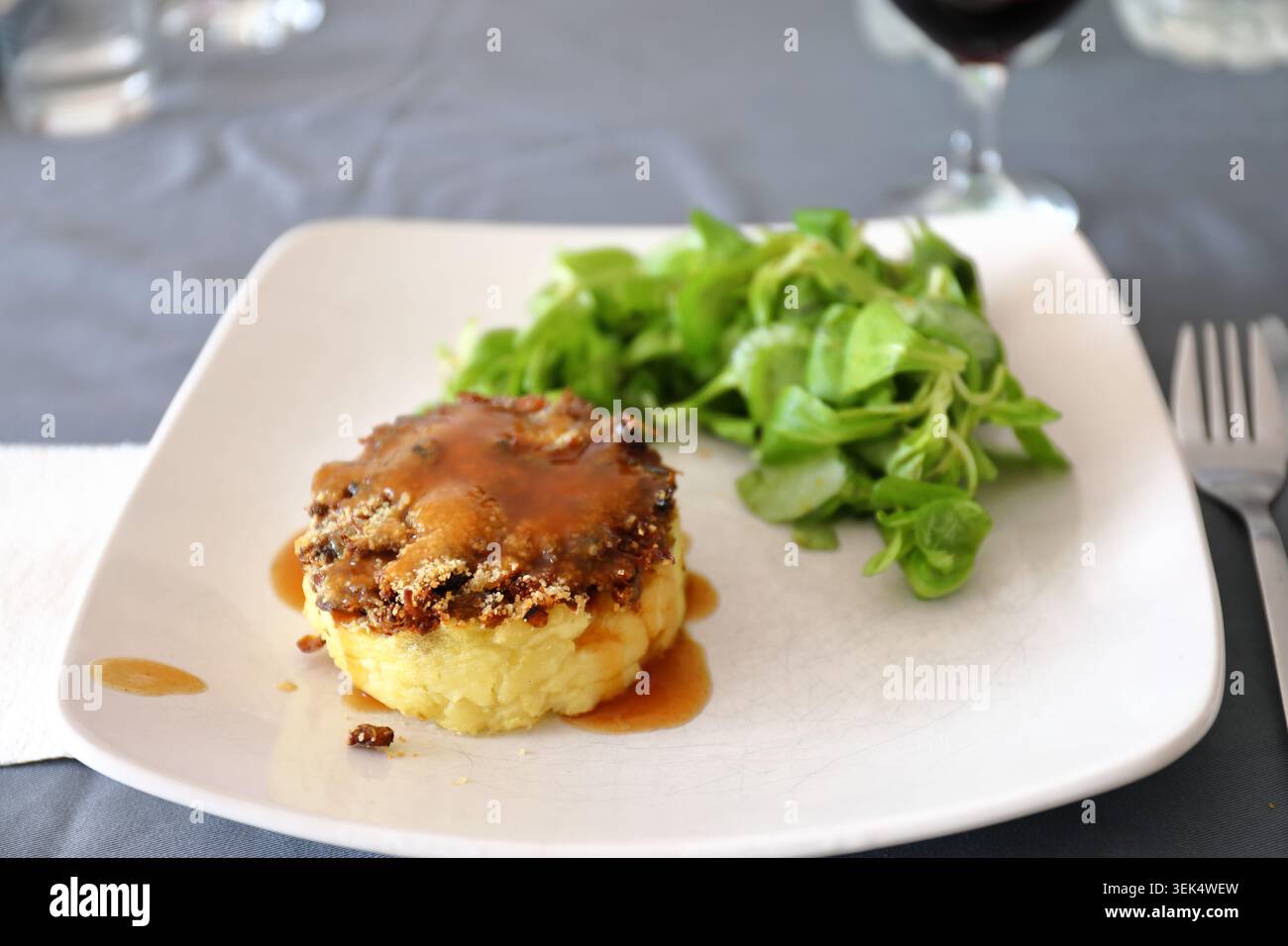 Torta di pastori d'anatra alla francese servita con purè di patate, salsa marrone e insalata verde fresca su un piatto bianco. Cibo gourmet con selezione di piatti Foto Stock