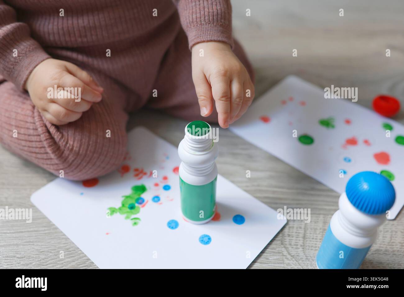 Primo piano con le mani del bambino che toccano la punta del marcatore a punti verde sulla carta da disegno. Attività didattica creativa per lo sviluppo di belle capacità motorie a casa. Reale Foto Stock