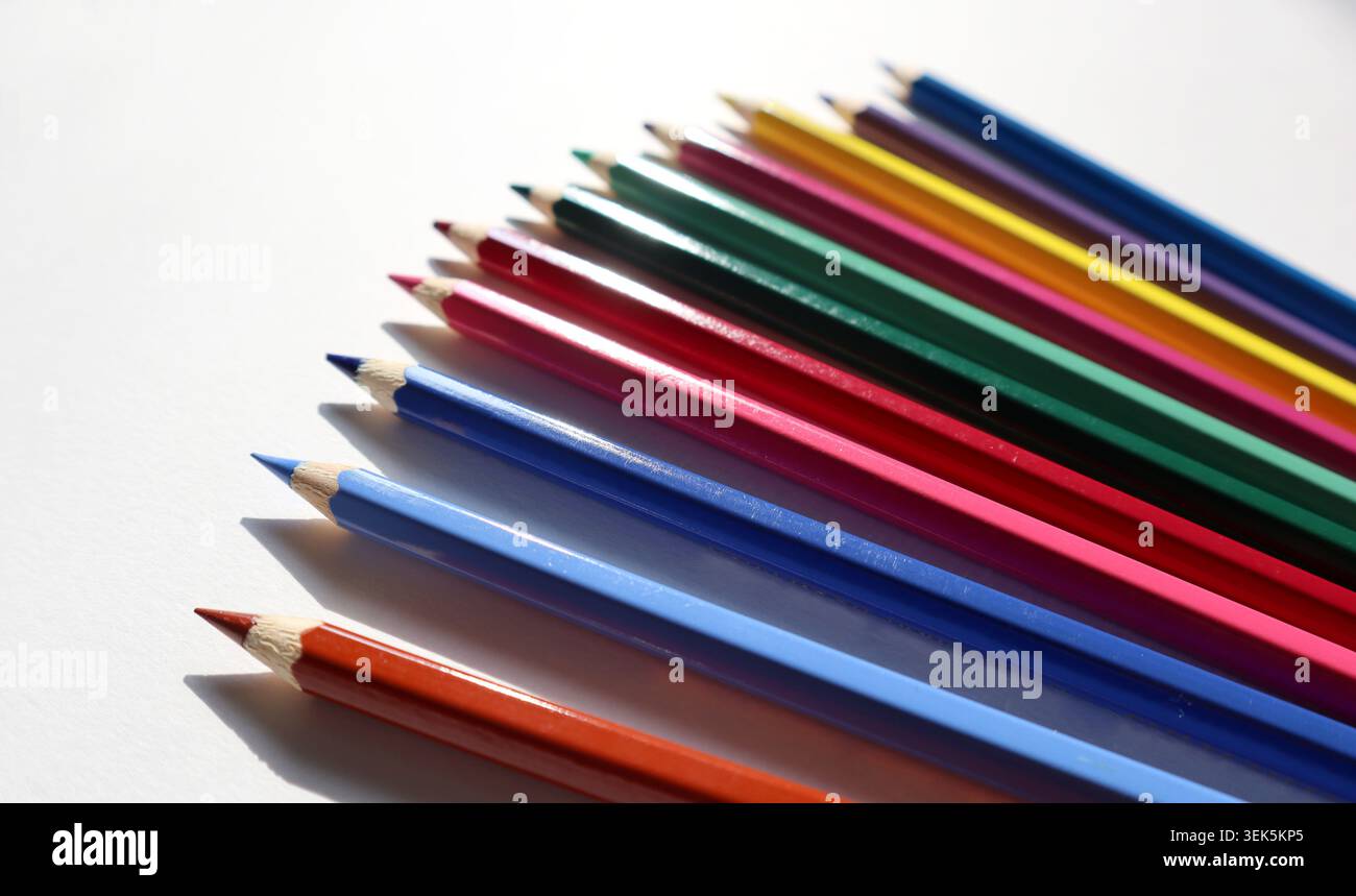 Un set di matite colorate è allineato in modo ordinato su una superficie bianca. La luce del sole mette in risalto i colori vivaci di ogni matita. Questa scenografia mostra gli strumenti per disegnare o colorare. Foto Stock