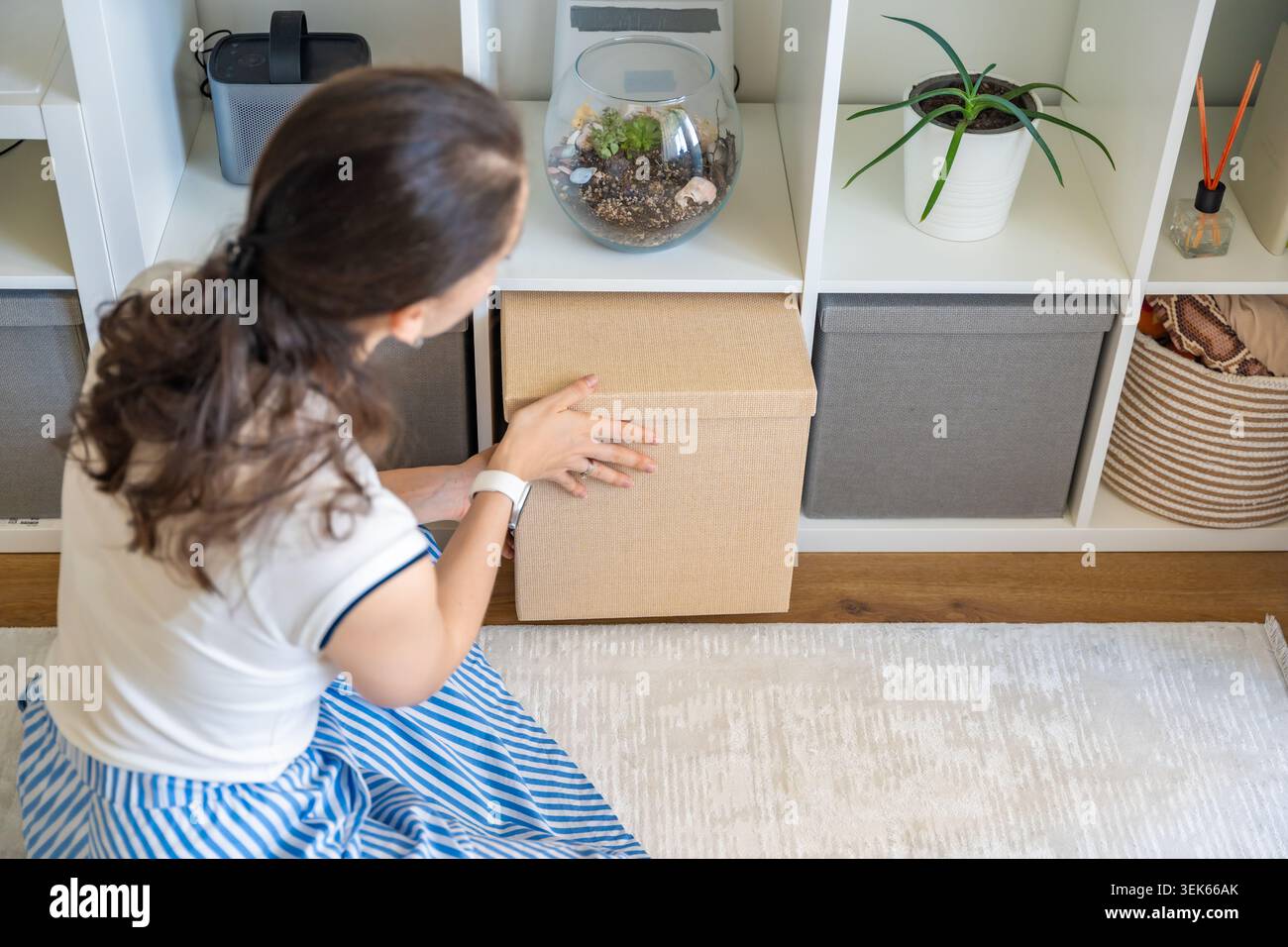Una giovane donna può riporre la scatola in tessuto in un ripiano minimalista a casa. Interni tranquilli e concetto di organizzazione sostenibile Foto Stock