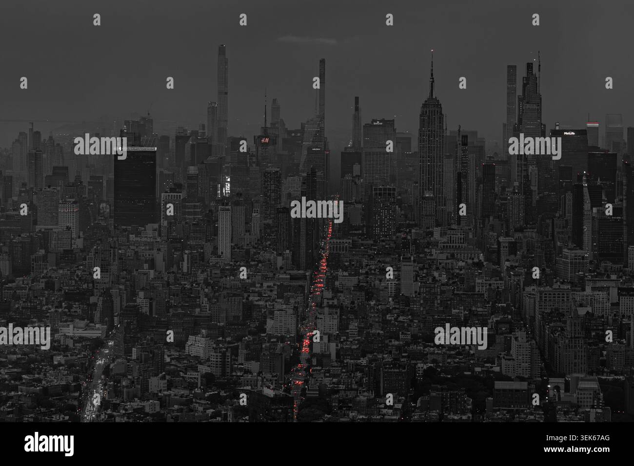 Skyline scuro della città con edifici alti e semafori rossi luminosi al tramonto, che mostrano una densa vista urbana in tonalità di bianco e nero Foto Stock