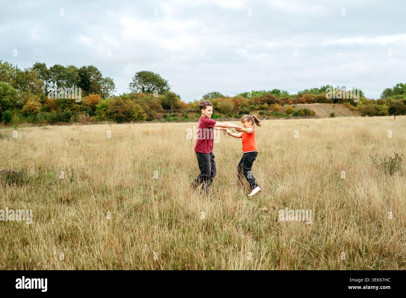 Fratello e sorella giocherelloni che girano insieme in un campo di campagna aperto Foto Stock