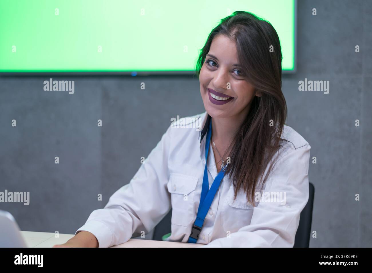 Una giovane e attraente agente di sicurezza con un rossetto scuro sorridente con sicurezza alla telecamera, indossando un'uniforme bianca con toppe in una t moderna Foto Stock