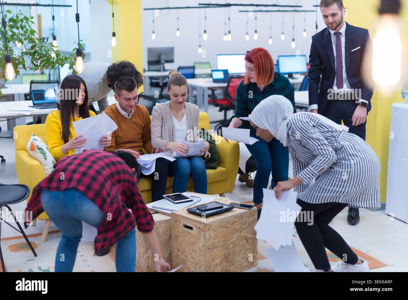Un gruppo variegato di nove giovani professionisti che posano insieme in un'area lounge di un ufficio moderno. Sono seduti e in piedi, sorridono alla telecamera, Foto Stock