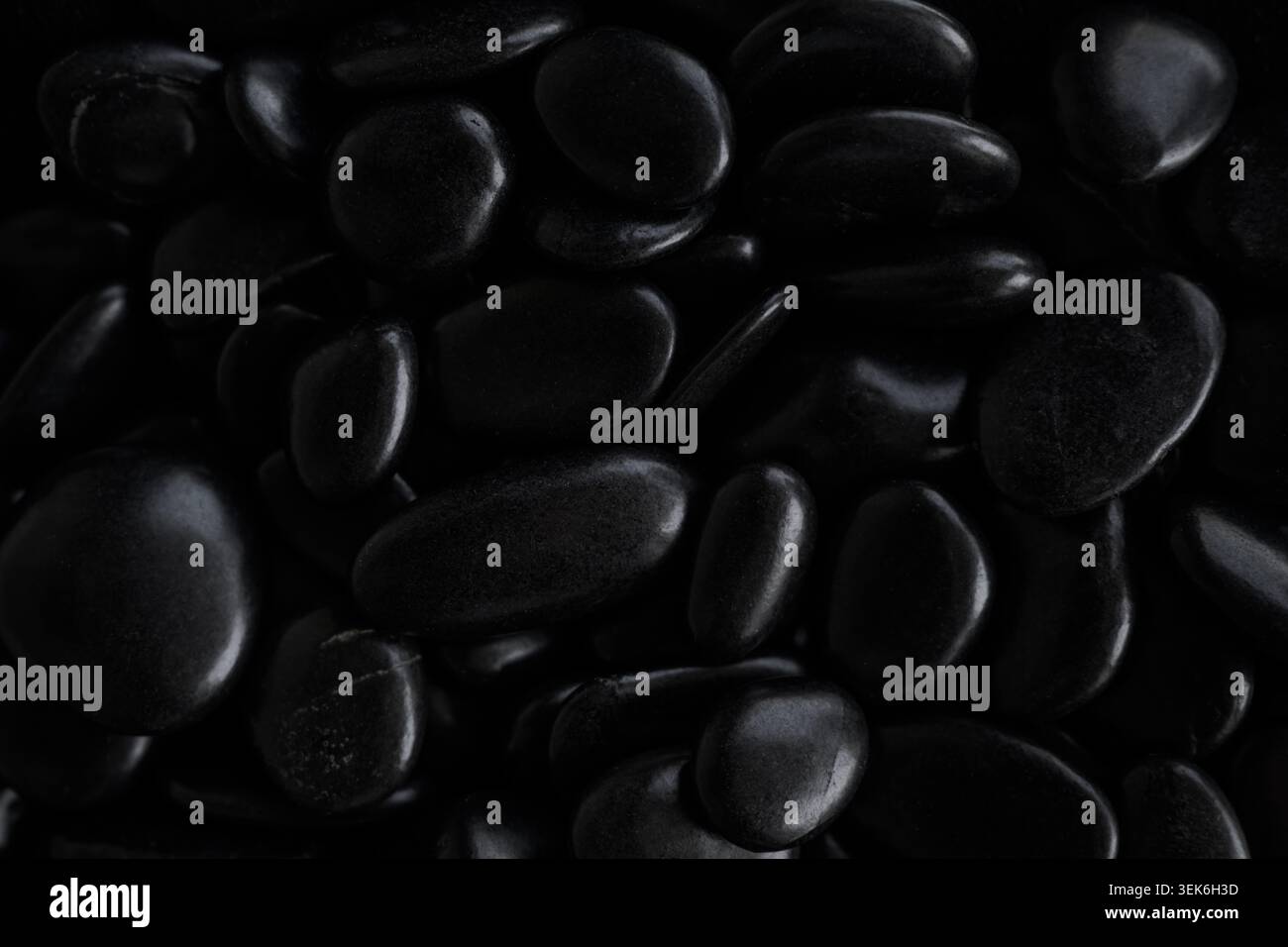 Primo piano di pietre nere lucide che creano una texture naturale astratta, un concetto di benessere e meditazione di lusso. Messa a fuoco selettiva. Foto Stock